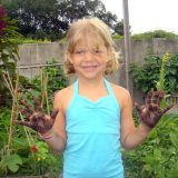 Little girl holding her hands up with dirt on them from the family garden