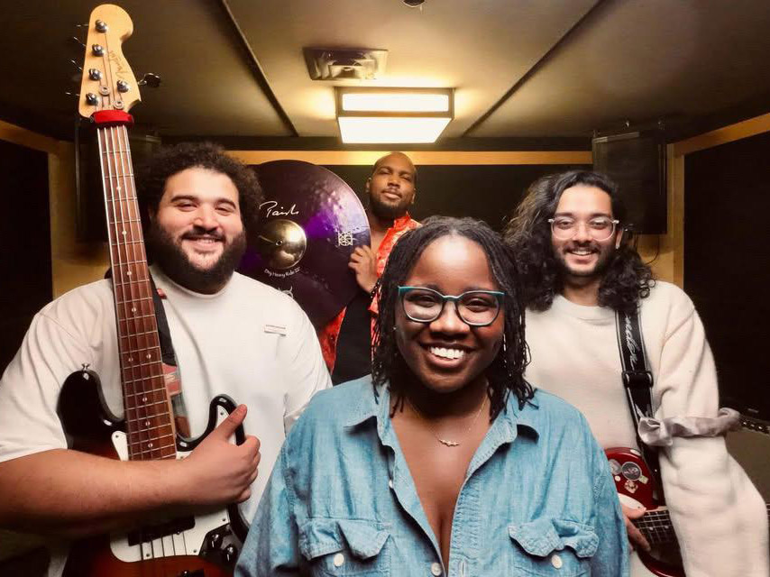 Four people with instruments pose for a band photo
