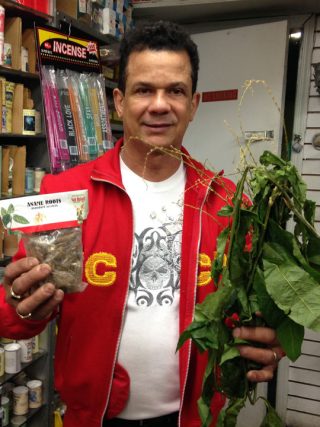 Man in red jacket holding a bag of roots and a green plant.