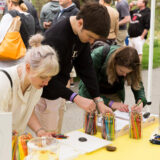 People gather around a yellow table outdoors to work with arts and crafts