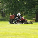 Garden staff working on motorized lawn mower on grass lawn.