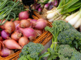 Baskets of produce including purple shallots, green broccoli, and white spring onions