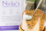 A clear container of granola with a large metal ladle inside, next to a sign labeled "Nicky's"