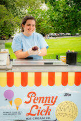 A person stands at an ice cream cart labeled "Penny Lick"
