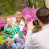 A parent and child pose for a photo surrounded by pink flowers
