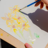 A person paints yellow flowers with a watercolor brush