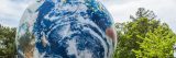 A giant globe set against a blue sky and several trees.