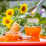 A jar of honey next to a piece of honeycomb in a bowl.