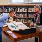 A man and woman looking at a botany book in the Library.