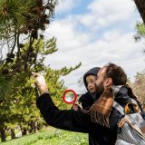 A young child being held by his father looking at a tree with a microscope.