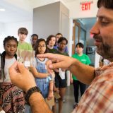 Man showing a plant specimen to young students