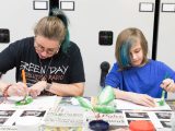 Two people paining green on paper leaves