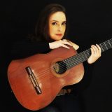 Lyra Kay holding an acoustic guitar.