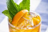 orange cocktail in a clear glass with cucumber, orange and mint accents.