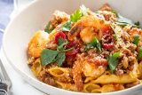 image of port and shirmp garganelli pasta in a white bowl in front of a glass of red wine, and a plate of cut bread