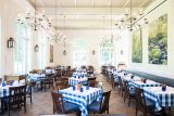 view of the dining space in the hudson garden grill with tables showing the blue and white checkered table cloths, tall arched windows, and brown and blue leather chairs