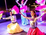 Close up of dancers with shiny and colorful clothing holding bright pink fans.