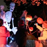 A life-size skeleton puppet surrounded by several children wearing puffy jackets during the night