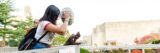 A person in a white shirt, with long dark hair, chucks a pale pumpkin from a rooftop