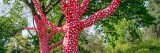 Trees wrapped in red fabric with white polka dots. More unwrapped trees and bushes can be seen in the background.