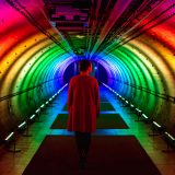 A person walking through a tunnel illuminated by a rainbow of lights.