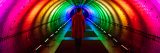 A person walking through a tunnel illuminated by a rainbow of lights.