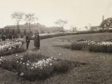 sepia image of two women and a man overlooking pathside plantings