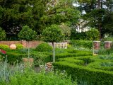 Long view of green potted trees, short red brick wall, green bushes in a designed pattern below tall green trees.