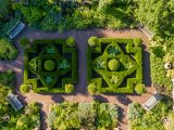 Aerial view of Herb Garden with brick paths, wooden benches in each corner, green bushes, and geometric shaped bushes in the center.