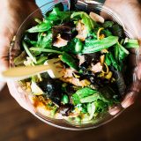 Hands holding a mixed salad in a bowl.