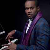 Harold O'Neal wearing a black and blue plaid suit jacket and a purple patterned scarf while playing piano