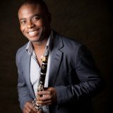 Head shot of Anthony McGill holdig a clarinet on a black backgroud