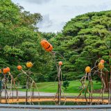 Several pumpkin-headed scarecrows made from fallen brances standing in a reflecting pool with small pumpkins floating around.