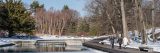 Three visitors wearing winter jackets walking beside the Native Plant Garden's reflecting pools. The surrounding forest and landscape is blanketed by untouched pure white snow.
