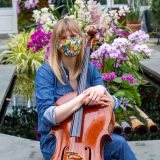 photo of woman Amanda Gookin seated with a cello in front of pink orchids