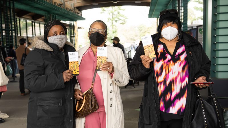 Three women wearing masks and holding ticket vouchers featuring Yayoi Kusama