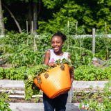 A child smiling and holding a bucket full of produce