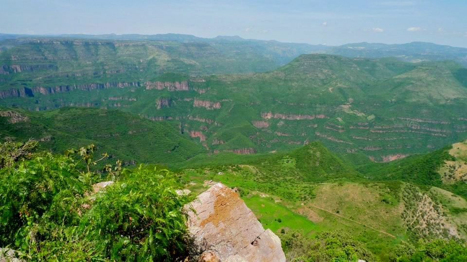 Photo from atop a cliff of green mountains and valleys interspersed with red rock