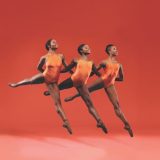 Photo of three dancers in orange outfits with an orange backdrop