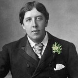 Black and white headshot of Oscar Wilde with a yellow flower pinned on his jacket