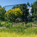 Photo of the exterior of the Infinity Mirrored Roomwith grasses in the foreground and a reflection of the landscape in the Infinity Mirror Room's exterior