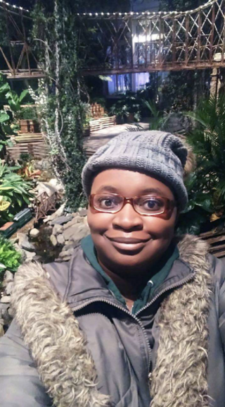 Adeola O., wearing warm winter clothes, takes a selfie of herself in front of the Holiday Train Show display