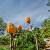 Three sculptures of stick figures with pumpkin heads on top