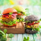 Plant-based burgers in a variety of shapes and colors sit on a cutting board, plants visible in the background