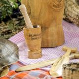 A wooden mortar and pestle sits on a table with various wooden utensils and a turtle shell