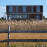 A square structure rises up in the background, with waving grasses and a wooden fence in the foreground