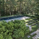 A terraced back yard, hemmed in with open forest, boasts lush green foliage planted around an in-ground swimming pool