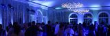 A large crowd of people gathers in a blue-lit ballroom, with chandeliers overhead