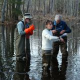 Aram JK Calhoun in a wetland with two men on each side of her