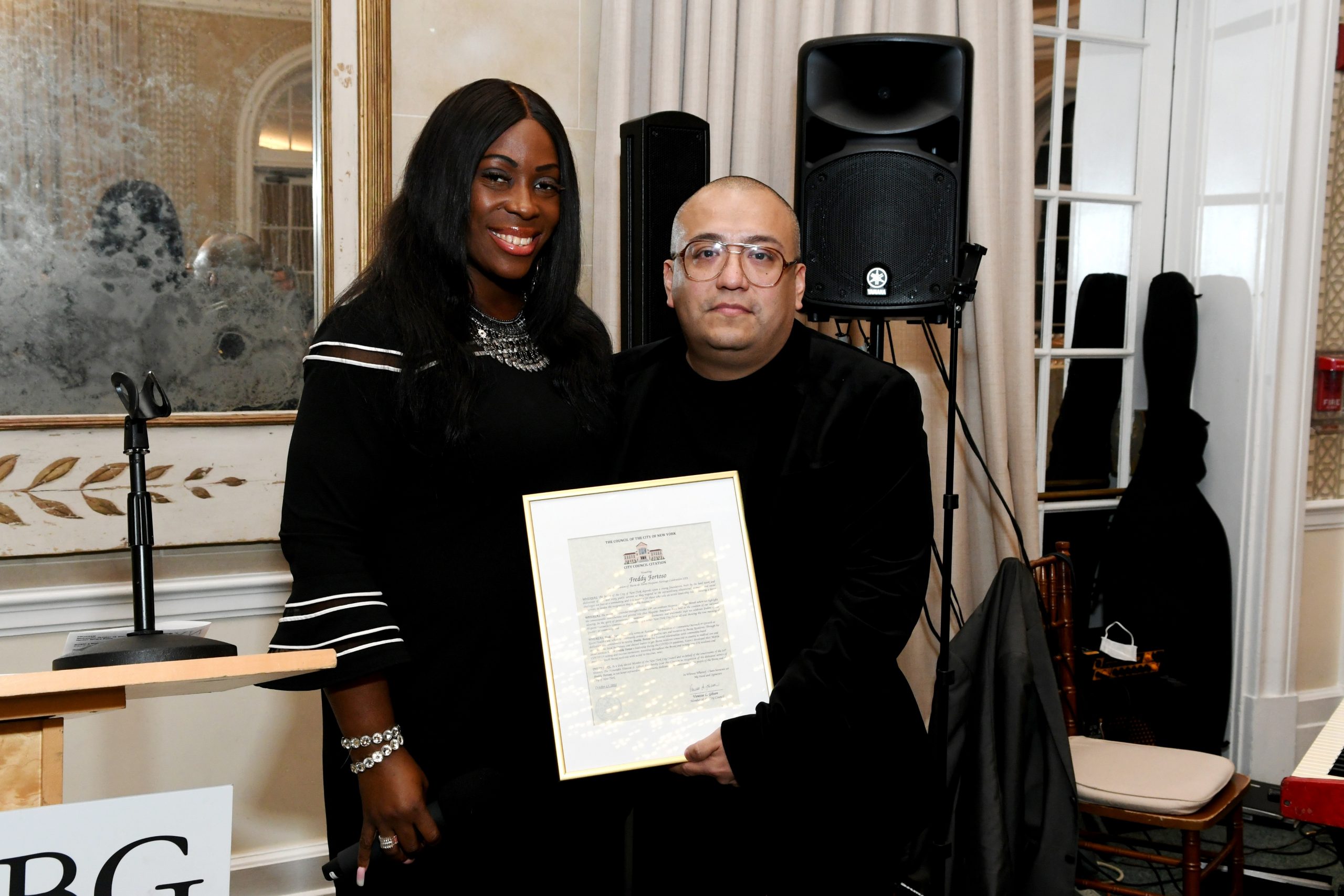 Two women in black outfits pose with a framed certificate